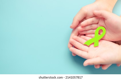 Lime Awareness Ribbon.Lymphoma Awareness Ribbon Lime Green On Child And Woman Mother Hand.Family Mother And Kid Treatment With Lymphoma.Patient Medical. Lymp.charity Campaign.Hope And Fight.background