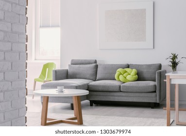 Lime Green Knot Pillow On Grey Corner Couch In Bright Living Room With Round White Wooden Coffee Table, Mockup Painting On The Empty White Wall