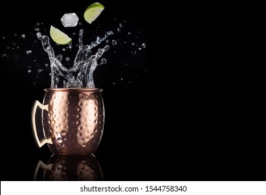 Lime And Ice Falling Into A Splashing Moscow Mule Cocktail Isolated On Black Background