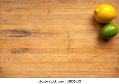 A lime and a lemon sit on a worn butcher block cutting board