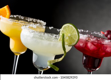 Lime Margarita, Orange Margarita And Cherry Margarita Cocktail Mix In Salt Rimmed Glasses Garnished With Slices Of Lime, Orange And Cherries. Focus On The Lime Slice