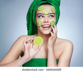 Lime Mask. Beautiful Girl Holding A Slice Of Lime And Smiling. Photo Of Girl With Flawless Skin In Green Towels. Skin Care And Beauty Concept