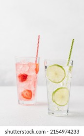 Lime mojito and strawberry lemonade with ice in tall glasses on light gray background. Berry refreshing summer drinks with straw