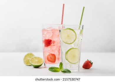 Lime mojito and strawberry lemonade with ice in tall glasses on light gray background. Berry refreshing summer drinks with straw