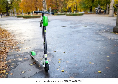 Lime Rental Electric Scooter Parked. A Green And Black Ride Sharing Lime E-scooter Stands On Sidewalk In Autumn Park, No People. Warsaw, Poland - October 17, 2021.