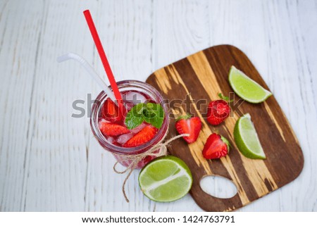 lime and strawberry slices on a plate and summer strawberry cocktail with mint and ice on a light wooden background