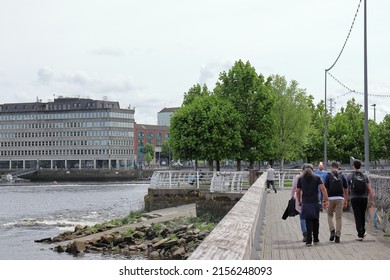 Limerick Ireland 05 07 2022: Group of friends walking along the river with trees and park ahead