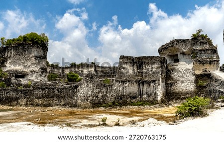 Limestone quarry with rugged cliffs and sparse vegetation under a blue sky.