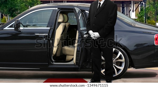 Limo driver standing next to opened car door with\
red carpet