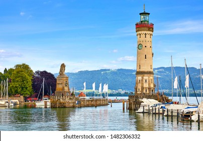 Lindau, Deutschland. Altes Leuchtturm mit Uhr in der Bucht. Antike bayerische Stadt am Bodensee. Monument mit Löwenstatue am Eingang zum Hafen, Yachten von Pfählen. Sommerlandschaft blauer Himmel.