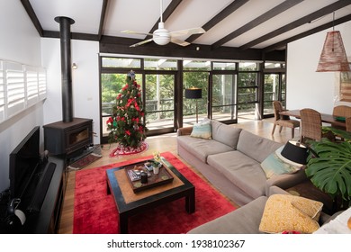 Lindfield, Sydney, Australia - Dec 9 2020: Lounge Room With Christmas Tree Decorations In Luxury Home With Sofas, Red Rug, Combustion Heater Fire Place Looking Out Onto A Deck Near The Bush.