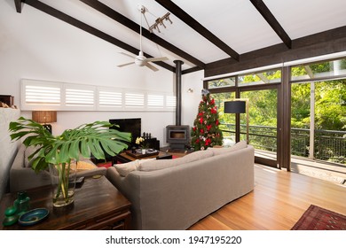 Lindfield, Sydney, Australia - Dec 9 2020: Lounge Room In Luxury Home With Christmas Tree, Decorations, Bare Rafter Ceiling, Sofas And Combustion Heater Fire Place, Looking Out Onto A Deck Near Bush.