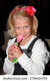 Lindstrom, MN USA September 11, 2010 Little Blond Haired Blue Eyed Girl Eating Pink Taffy. Red Flower On Her Headband.