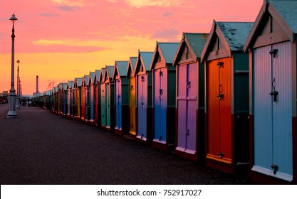 a line of 30 beach huts with a diminishing perspective, the nearer beachhuts are big, lamp post and promenade, brighton seafront