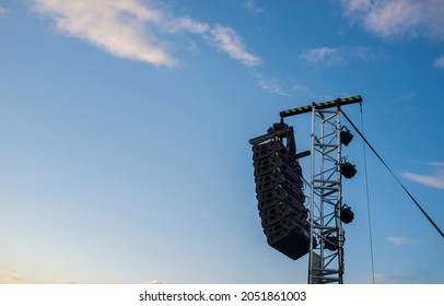 Line array speaker system hanging from pole during daylight performance. Sunset blue sky background