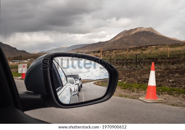 Line of\
cars waiting for their turn to drive in reverse traffic during road\
repair work. Beautiful mountains of Connemara in the background.\
Transportation industry. Cloudy\
sky