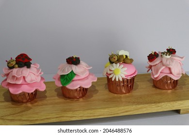 line of cute pink cupcakes with candy bees and beetles on top.