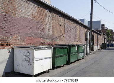 A Line Of Dumpster Sit Along An Old Back Wall In An Urban Alley.