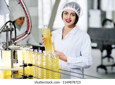 line of food production of refined sunflower oil. Girl worker at a factory on a conveyor background with bottles of vegetable oil.