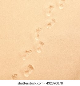 Line Of Footprints Walking Away From The Camera Through Golden Beach Or Desert Sand Diagonally Across A Square Frame In A View From Above