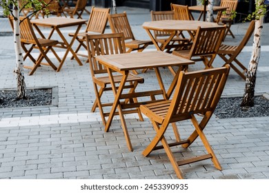 A line of hardwood folding tables and chairs with wood stain on a brick sidewalk, creating a cozy outdoor seating area - Powered by Shutterstock