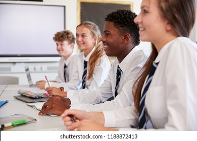 Line Of High School Students Wearing Uniform Sitting At Desk In Classroom