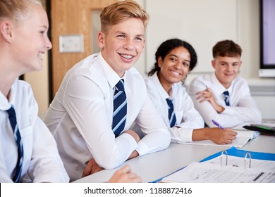 Line Of High School Students Wearing Uniform Sitting At Desk In Classroom