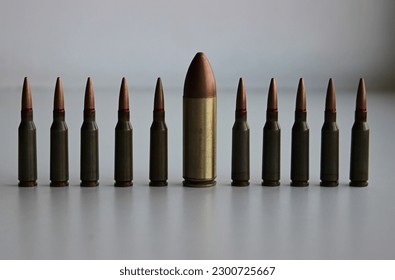 A line of identical regular caliber bullets with one huge large caliber bullet front view detailed stock photo

