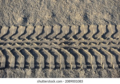 Line Of Marks Of Car Or Truck Tyres Printed In Sand Of Beach In Canary Islands. The Pattern Of Tread Of Tyre Prints, Structure Of Sand Are Highlighted By Shadows From The Sun Rays. Close Up Macro View