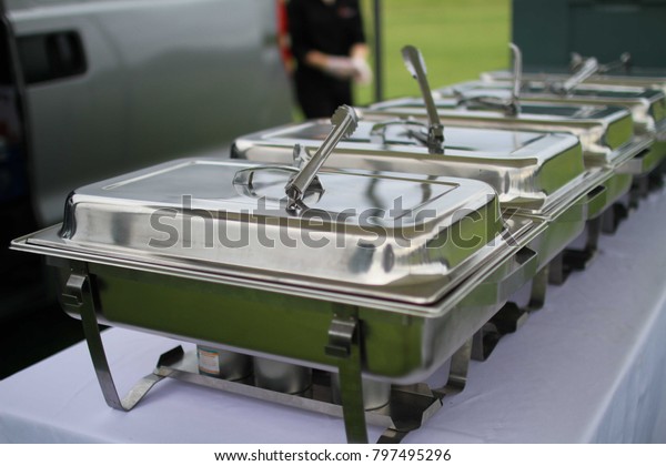 Line of metal containers for outdoor buffet at a park\
in front of a van
