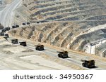 A line of monster dump trucks carry 250 ton loads of rock out of an open pit mine.
