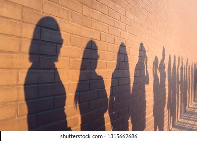 a line of shadows of people lined up against a red brick wall. Stand in a queue to the changes - Shutterstock ID 1315662686