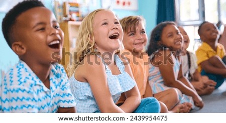 Line Of Smiling Primary Or Elementary School Students Sitting On Floor During Classroom Lesson