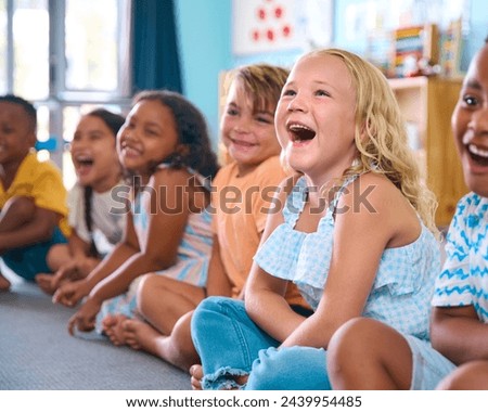 Line Of Smiling Primary Or Elementary School Students Sitting On Floor During Classroom Lesson