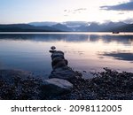A line of stones jutting into Lake McDonald in Glacier National Park with the rugged Livingston Mountain Range and a small motor boat in the background. Photographed at dawn.