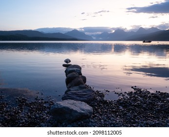 A line of stones jutting into Lake McDonald in Glacier National Park with the rugged Livingston Mountain Range and a small motor boat in the background. Photographed at dawn.