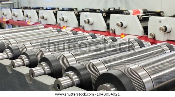 Lined up magnetic cylinders for die cut on rotary\
printing press. Magnetic cylinder for flexo rotary die cutting.\
Magnetic roll and in-line press machine in background. Cylinder for\
cutting dies.