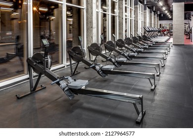 Lined modern rowing machines and treadmills by window in spacious, empty gym interior. Special equipment for physical training. Sport, fitness - Powered by Shutterstock