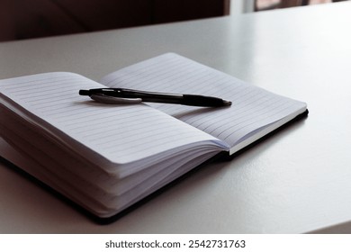 A lined open notepad book with black pen placed on a white isolated table. Idea of planning, back to school, business concept, brainstorming, future, mapping, diary concept.