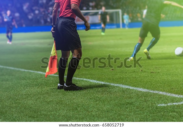 Lineman assistant referee with flag Officiate\
soccer game beside soccer\
field.