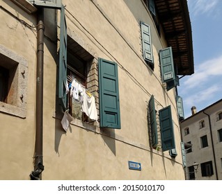 Linen Hanging Out To Dry On The Shuttered Window Of An Old Town Building In Italy. Public Traffic Sign Which Translated Means One Way, Bottom Right.