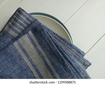 Linen striped blue napkins, towels on a plate. Wooden background.