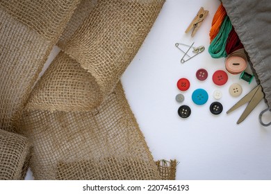 Linen Textiles, Scissors And Sewing Supplies On White Table. Sewing Composition With Threads, Loose Hemp Fabric, Scissors, Buttons, Needles And Other Sewing Accessories On White Background.