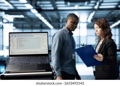 Lines of code on laptop screen in data center with programmers in blurry background. Close up of programming language on notebook display used by IT experts inspecting server clusters