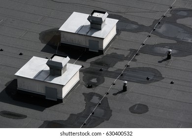 Lines of grey and black asphalt on the flat roof. Cables and devices of ventilation and airing on the top of the building. View from above.