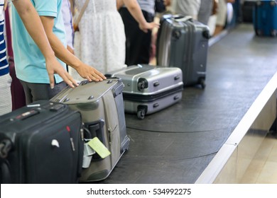 Lines Of People Waiting For Their Baggage At Baggage Claim At Airport With Focus On Man Hand Touching Baggage