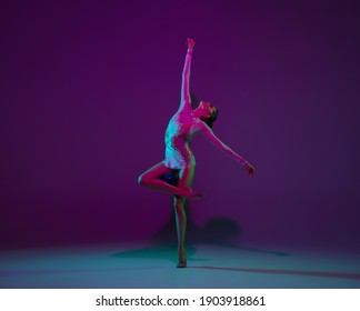 Lines. Young female athlete, rhythmic gymnastics artist dancing, training with ball isolated on purple studio background in neon light. Beautiful girl practicing with equipment. Grace in performance.
