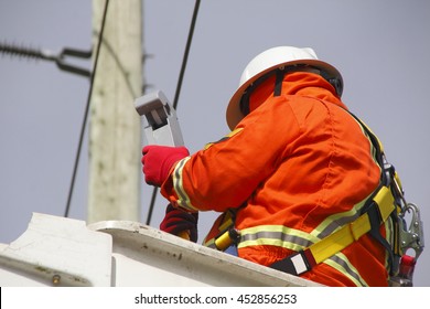 A Linesman Checks Data On A Wireless Voltage Reader Used To Gauge Current Through Electric Lines/Hydro Electric Linesman Checks Voltage Reader/A Linesman Checks Data On A Wireless Voltage Reader. 