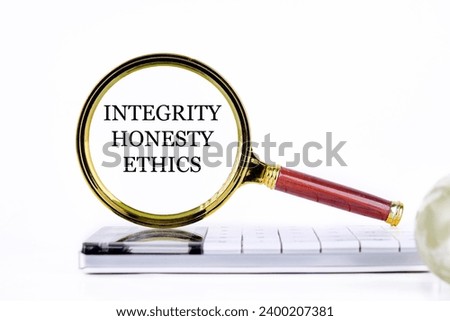 lINTEGRITY HONESTY ETHICS ettering through a magnifying glass on a calculator and part of a magic ball in the foreground without focus