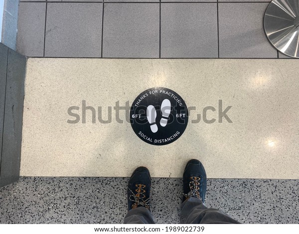 Linthicum Heights, Maryland, US - June 6,\
2021: Waiting in a socially distanced queue line at Baltimore\
Washington International Airport rental car terminal with round\
sign with footprint\
instructions